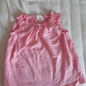 Rosa klänning med små vita hjärtan. - Aldrig använt och är inte så skrynklig. Väldigt bra resårband runt halsen samt båda ärmarna och kan töjas ut Väldigt bra. Har små vita hjärtan på både fram- och baksidan.