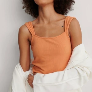 Oranget linne från Nakd  - Oranget ribbatlinne från Nakd med en axeldetalj. Säljer på grund av kommer inte till användning. Storlek Medium, pris 100kr exklusive frakt. använt fåtal gånger 