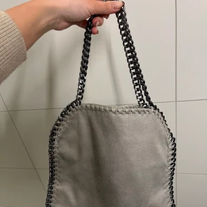 Väska m. kedja - Grå väska med silverkedja, helt oanvänd och är suuuper fin. Kan användas både över bröstet men också hållas i handen elr hängandes på armen. Väldigt praktisk.