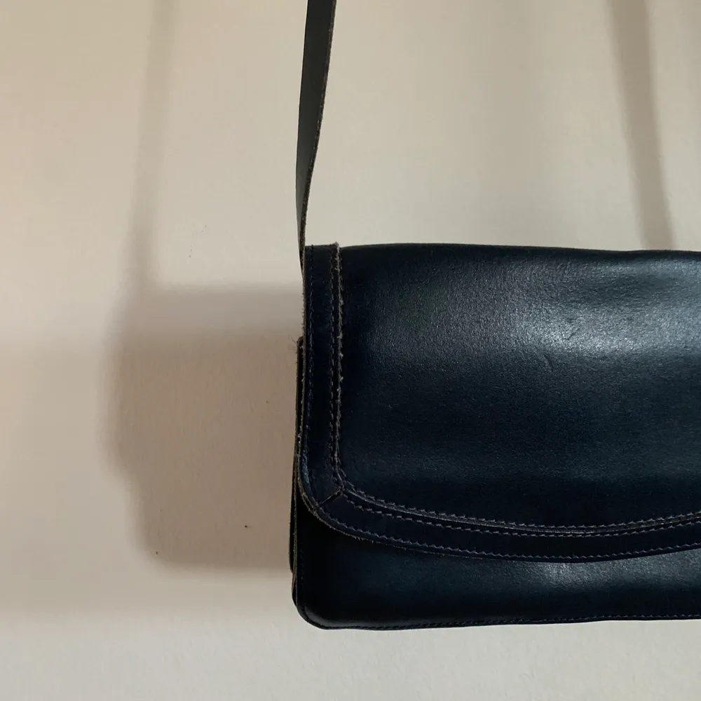 Mörkblå (färgen är svår att se på bilden) handväska med långt, justerbart axelband. Tre fack innuti, ett med dragkedja. Mått: 20x14x4 cm (djupet går att förstora) Axelbandets mått: va 110cm🌟. Väskor.