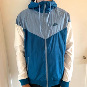 Nike jacka, strl M - Nike vindjacka med mörkblå och ljusblå. Jackan är i fint skick trots att den är använd några gånger. Endast en liten fläck på framsidan (se första bilden). 