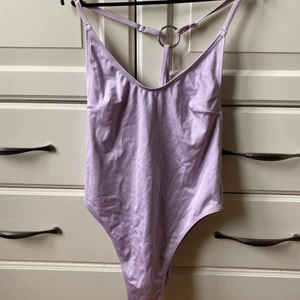 Baddräkt - Baddräkt i metallisk violett färg som skimrar i solen. Köpt på H&M. Sparsamt använd. Storlek XS/S. Frakt ingår i priset.