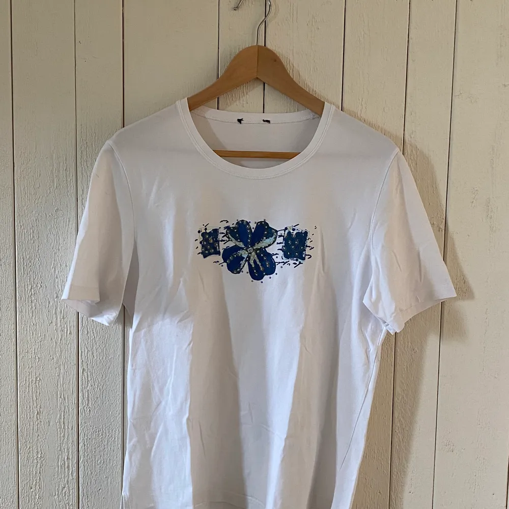 Vit t-shirt med blåa blommor i paljetter. Passar som storlek M. Märke är okänt. Mycket bra skick.. T-shirts.