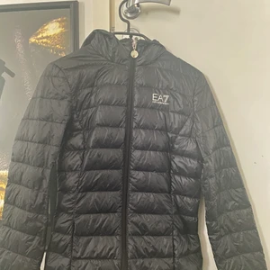 Emporio Armani jacka dam - Svart dun jacka från emporio armani dam. Jackan är i passform. Alltså passar den lite tajtare runt midjan. Använt några fåtal gånger men är i jättebra skick, inga hål osv. Säljer pga den inte kommer till användning. Passar perfekt till hösten/början av vintern. Säljer för 900-1000, Köpt för 1500kr❤️ pris kan diskuteras