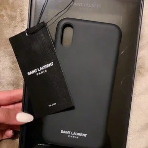 ÄKTA SAINT LAURENT IPhone XS skal  - Svart, stilrent äkta iPhone skal i silikon från Saint Laurent för XS modellen. Köpt på hemsidan, skickas med boxen den kom i, taggen sitter kvar på boxen. Slutsåld överallt. Använt fåtal gånger. Säljs pga inköp av ny mobil. 