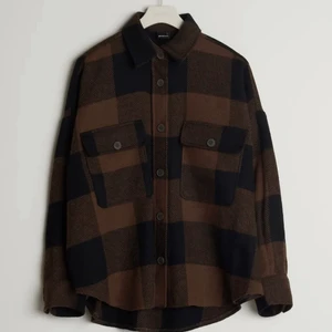 Brun skjorta - Rutig skjorta med bröstfickor. Skjortan är brun och långärmad och har en krage. Den har knappar framtill och på fickorna. Skriv om intresserad.