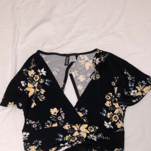 Crop top med blommor - En crop top från H&M, helt oanvänd. Den har cut out back vilket är super trendigt just nu! Flowiga korta armar. Strl xs 
