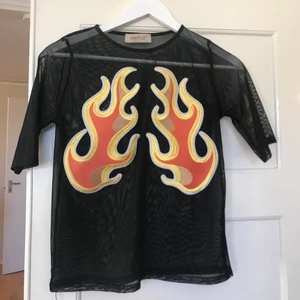 Tröja med eld - Tröja med eldtryck. I material mesh (genomskinlig). Köpt secondhand. Storlek står ej angivet men skulle bedöma den som en större S, alternativt M. Tyget är stretch så funkar för det flesta! Jag har aldrig använt. Fint skick. Frakt tillkommer 🌹