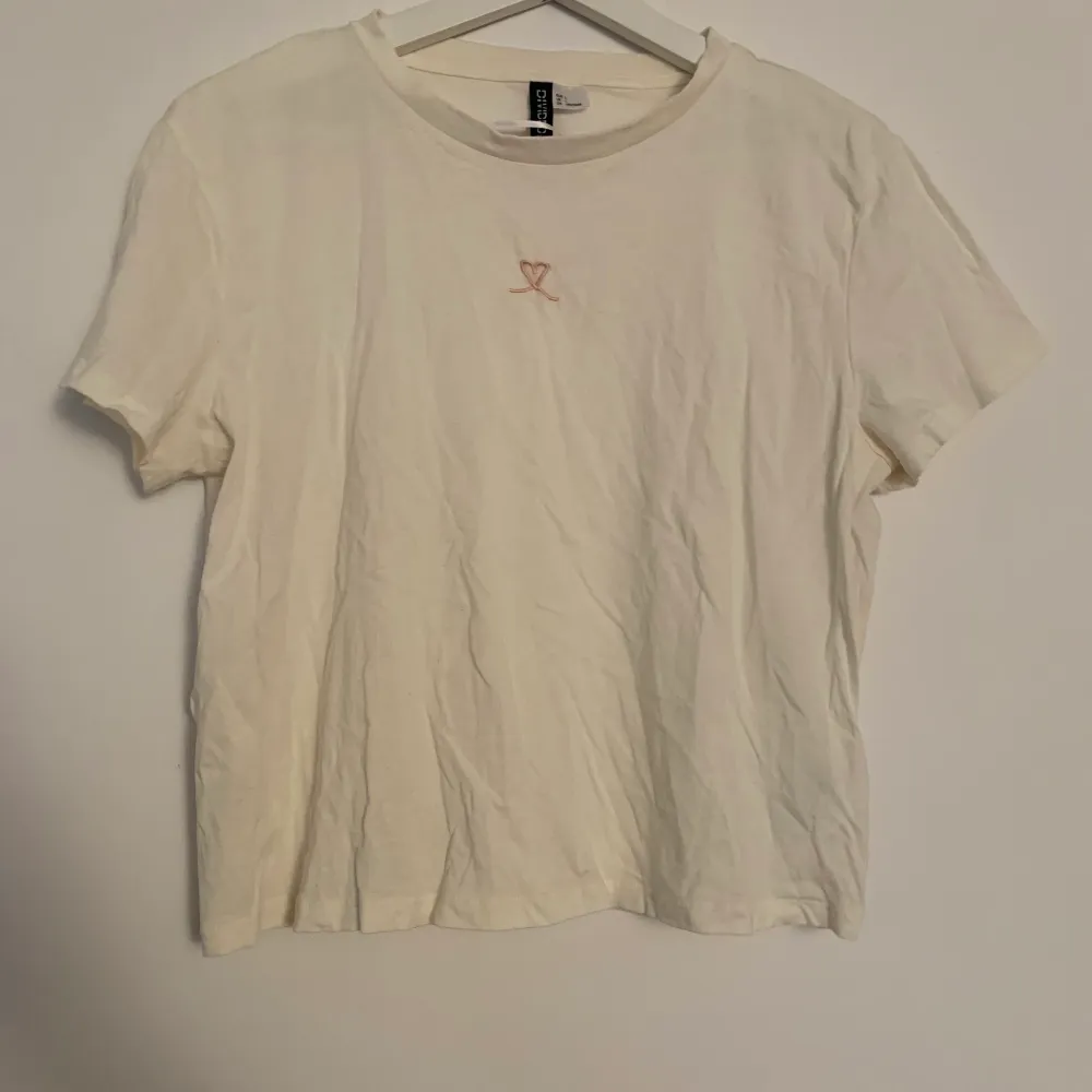 Vit/ljusbeige t-shirt från H&M med ett rosa hjärta. Storlek L men passar även S-M beroende på hur man vill ha passformen. . T-shirts.