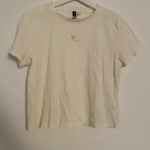 Vit/ljusbeige t-shirt från H&M med ett rosa hjärta. Storlek L men passar även S-M beroende på hur man vill ha passformen. 