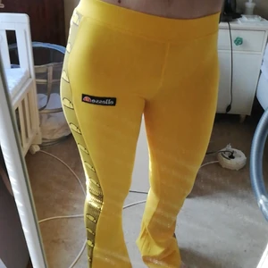 Ellesse flare strech byxor strl. 34 - Tajta gula strech byxor med svarta revärer med signaturloggan på sidan av byxorna, helt oanvända med prislappen kvar. 