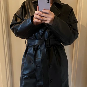 Kappa i imitationsskinn  - Det är dags för mig att inse att denna fina kappa i skinnimitation behöver hitta sitt nya hem, perfekt att möta våren i! Sparsamt använd och i fint skick! Kappan mäter 92,5 cm är lång (mätt från nedanför nacken/kragen), och på mig som är lite under 160 cm så slutar den strax nedanför knäna. Dock har den några små ”fläckar” i lädret om man synar den noga, dessa syns knappt när man har den på sig. Om priset känns alldeles för dyrt, testa pruta vettja!