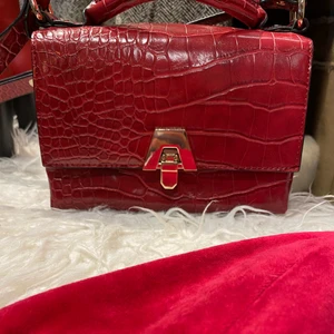 Fin röd retro väska från ZARA - Supersnygg fauxläder väska från ZARA. Säljes inte längre utan denna är ganska gammal. Finns även ett axelband och ett mindre ”handtag” på väskan. 