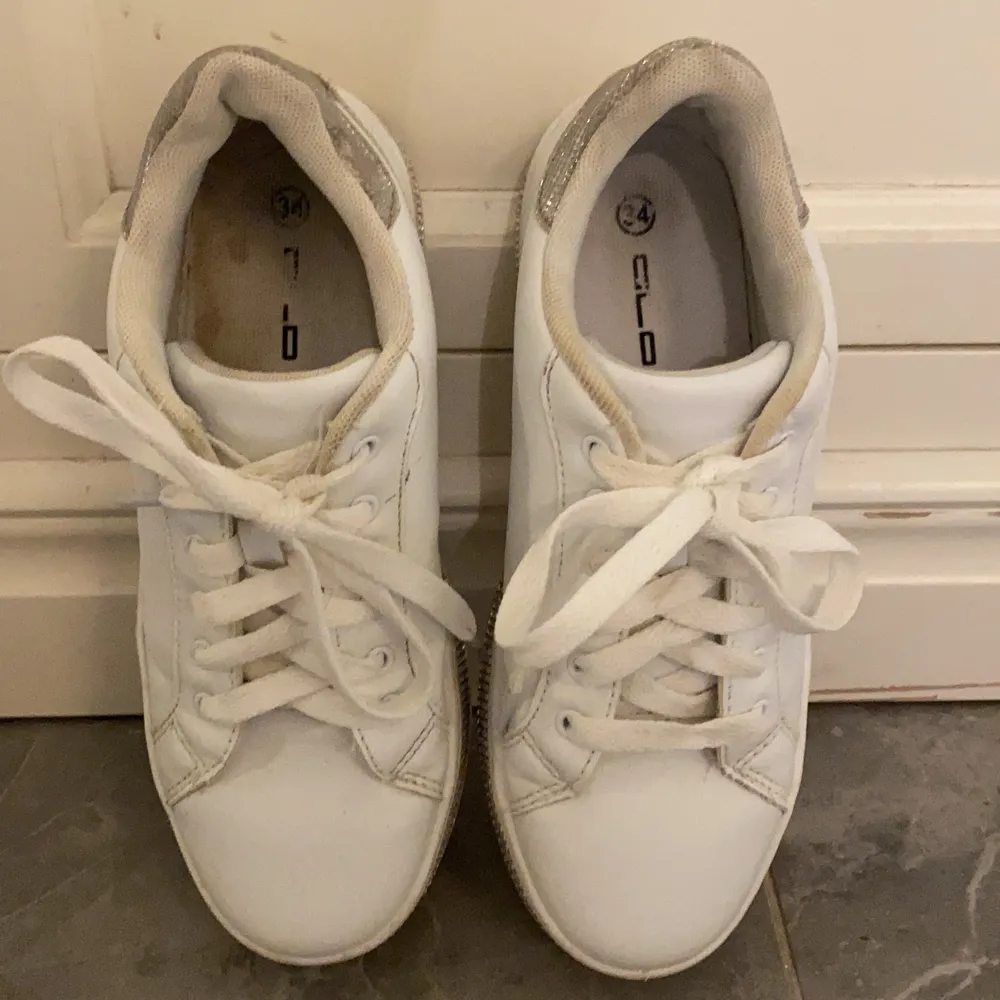 Detta är ett par vita sneakers med glitter på sulan i storlek 34. Skorna är stora i storlek så passar även dem flesta med 35. Dem är lite slitna inuti och dem har tappat några diamanter men det är inget man ser eller tänker på! . Skor.