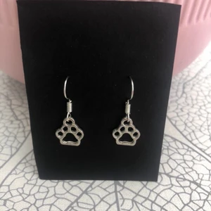 Örhänge med tass - Söta nickelfria örhängen med tassberlocker på som säljs till ett billigt pris. Såklart aldrig använda. Om du är intresserad av att köpa något av mina smycken kan du göra det här eller kolla in hemsidan som du hittar på instagramen glossy.shop.se där det även finns ett större utbud då jag inte lagt upp allt här än🌸💞🤟💖