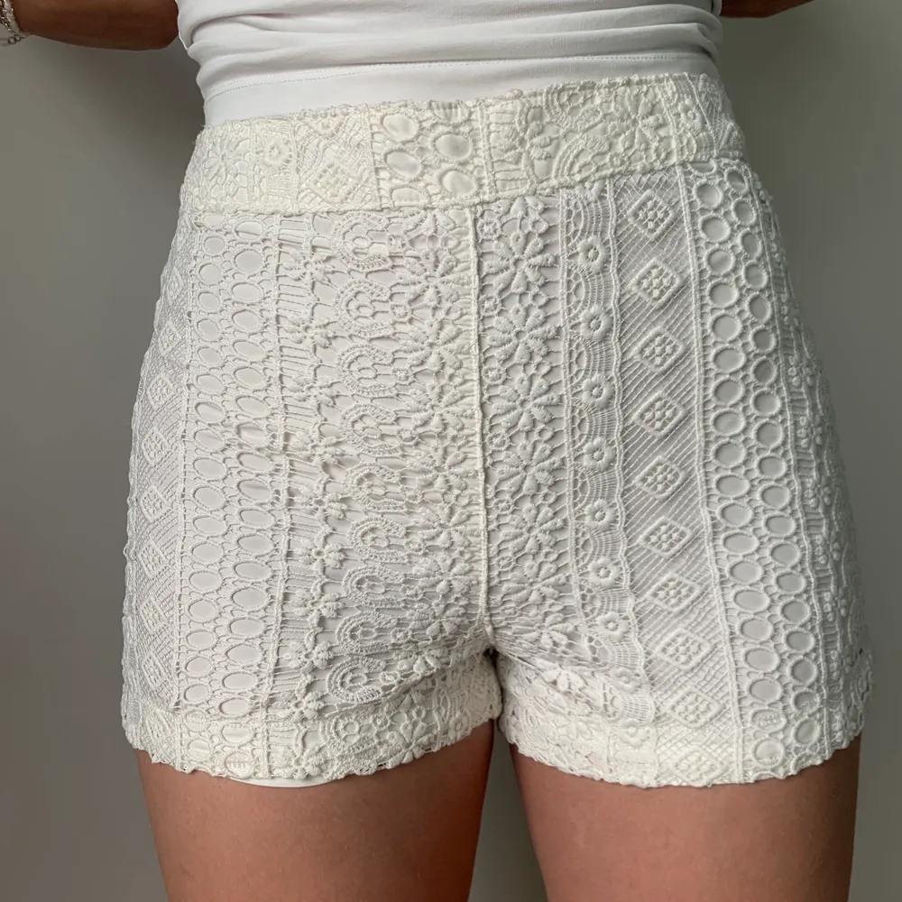Ett par vita shorts med spets detaljer. Dragkedja på vänster sida för att få av och på. Shorts.