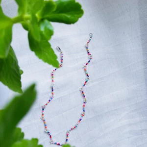 Pärlhalsband ”Multifärgad blomster” - MULTIFÄRGAD BLOMSTER är ett pärlhalsband som är ca 40cm långt. Den har en karbinhake som håller ihop smycket.