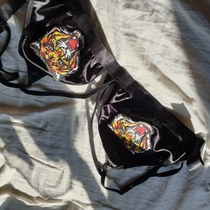 Häftig bralette - Säljer min svarta bh, bralette, med ett tigerhuvud fast broderat på brösten. Den är skön men jag anvönder aldrig den, jag tycker att hundhuvudet kunde ha blivit på sytt bättre men annars inget konstigt med den. Kommer inte ihåg vart den är köpt ifrån! Den är i storlek M, är lössittande på mig som är en M/L. Du som köper står för frakt 😊