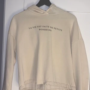 Beige ”hoodie” med text  - Säljer denna beige luvtröja med text på från Gina tricot. Strl xxs, använd fåtal gånger och bra skick. Liten fläck på men syns knappast förutom nu när jag hade blixt på. Går att knyta ner till.