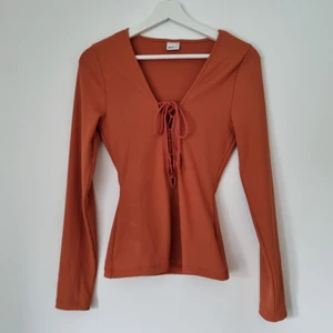 Ribbad top med snörning, Gina Tricot (M) - En ribbad, terrakottafärgad top med snörning från Gina Tricot i storlek M (passform M). OBS snörningen/urringningen går till ovanför naveln/mid torso.