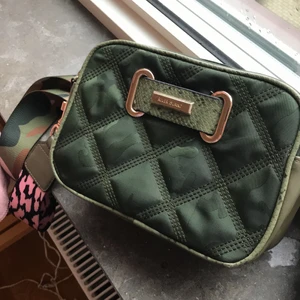 River island väska  - Nu har jag tänkt att sälja min militärgröna axelväska som jag har köpt i England 2019 för ca 900 SEK. Väskan är inte andvänd över huvudtaget och de är anledningen till att jag säljer den. Den skulle passa jätte fint nu när det blir varmare ute under våren men den passar såklart till alla årstider. Väskan är grön med ett band som har rosa detaljer vilket gör väskan unik. Bandet går att byta om man så vill. Vid frågor eller funderingar så är det bara att kontakta💚fler bilder kan skickas om önskas 