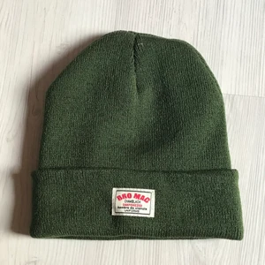 Beanie  - Asskön mörkgrön beaine med en tyglapp på framsidan. 