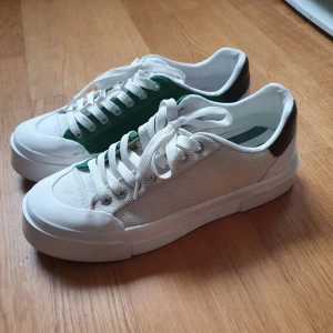 H&M samarbete med Good News Sneakers - Ett par sneakers från H&Ms samarbete med Good News i storlek 37. Yttre sidan av skon är naturfärgad och insidan grön, grövre platåsula. Använda endast en gång. Ordinarie pris 499 kr.