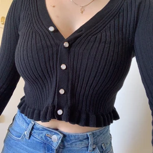 Svart kofta - Gullig svart cardigan i croppad modell med vita knappar och volangkant.