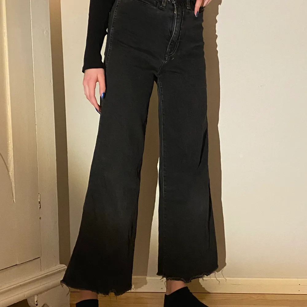 Ett par svarta högmidjade jeans med fransar längst ner. Jeans & Byxor.