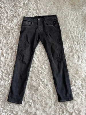 Svarta slim fit jeans från Replay - Snygga svarta slim fit jeans från Replay med klassisk femficksdesign och silverfärgad knapp. Jeansen har diskreta kontrastsömmar och är tillverkade i mjukt denimtyg. Perfekta för en trendig och avslappnad look.