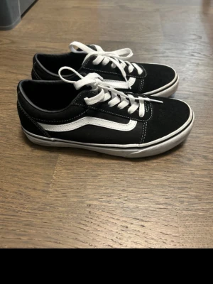 Svarta Vans Old Skool sneakers - Klassiska Vans Old Skool sneakers i svart med vit sula och vit sidestripe. Skorna har snörning, låg profil och är tillverkade i mocka och canvas. Perfekta för en streetwear-look och funkar året runt. Lite smutsiga men inga skavanker.