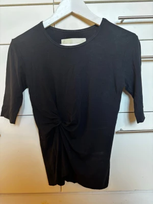 BACK Svart topp i viskos med knutdetalj storlek S - BACK (vintage 2014). Svart topp med rund hals och trekvartsärm. Toppen har en snygg knutdetalj framtill som ger en cool twist till looken. Vidkos. Jättefint skick! Storlek S