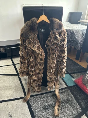 Pälskappa från Vabene - Unik brun kappa från Vabene med pälsmönster i spiralformade detaljer och bred pälskrage. Kappan har knytskärp i midjan och knappar. Perfekt för dig som vill sticka ut med en statementjacka i höst och vinter. Nypris ligger på 4000kr, Vårt pris är 1500kr. Priset går att diskuteras men ej hugg i sten 🪨 