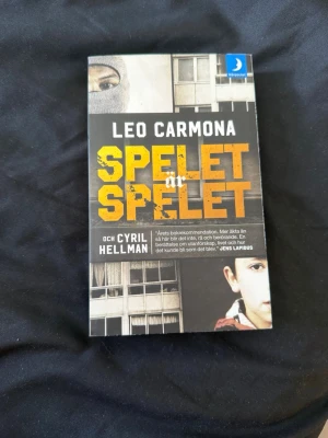 Spelet är spelet av Leo Carmona - En spännande pocketbok med titeln 'Spelet är spelet' av Leo Carmona och Cyril Hellman. Omslaget är svart och gult med bilder av fönster och ansikten, vilket ger en rå och urban känsla. Perfekt för dig som gillar verklighetsbaserad skönlitteratur.