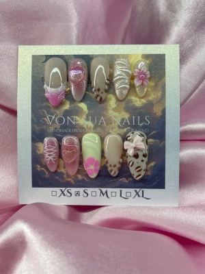 RosyMilk (S);Medium Almond - Handgjorda press-on naglar i olika designer med nude, rosa och glitter. Setet har detaljer som 3D-blommor, leopardmönster, hjärtan och snörningsmönster. Naglarna är medium lång mandelformade och tillverkade i S: 15 mm, 11,5 mm, 12 mm, 11 mm, 9 mm . Perfekt för dig som vill ha unika och trendiga naglar.