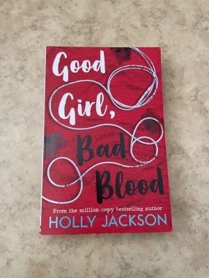 Good Girl, Bad Blood av Holly Jackson - En spännande pocketbok med röd framsida och vit samt svart text. Omslaget har ett slingrande vitt snöre som motiv och titeln är tryckt i stora bokstäver. Perfekt för dig som gillar mysterier och ungdomsromaner.