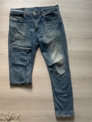 Levi’s 502 W36 L34 - Klassiska blå jeans från Levi's med raka ben och femficksmodell. Jeansen har en snygg tvätt med slitningar på låren och en liten röd Levi's-tag på bakfickan. Tillverkade i denim och har normalhög midja.