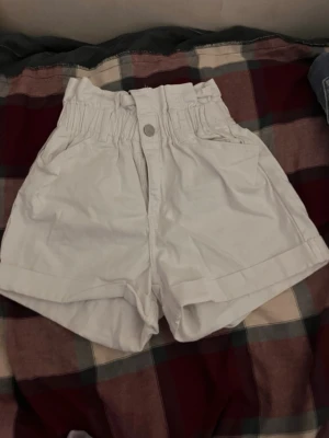 Vita high-waist shorts med resår - Snygga vita shorts med hög midja och resår i midjan. De har två fickor fram och två bak, samt en knapp och dragkedja framtill. Helt nya och oanvända.