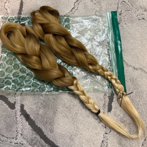 Syntetiskt hår blond - Snygg och lång fläta i syntetiskt hår i en naturlig blond nyans. Perfekt som håraccessoar för att skapa en cool look eller cosplay. Flätan är tjock och har en mjuk, glansig finish. Enkel att fästa med snoddar i ändarna.