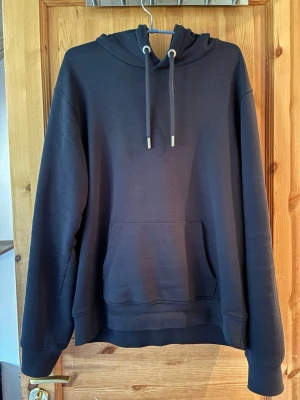 John Henric  hoodie  - En stilren blå hoodie med huva och snörning. Klassisk känguruficka framtill och ribbade muddar vid ärmslut och nederkant. Perfekt för en avslappnad look ny skick endast använd 1gång 