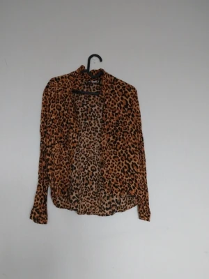 Leopardmönstrad skjorta i tunn polyester - Snygg skjorta med leopardmönster i bruna och svarta toner. Skjortan är långärmad och har en avslappnad passform. Perfekt för dig som vill sticka ut med ett djuriskt print. Tillverkad i tunn och luftig polyester.