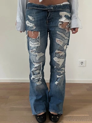 Blå slitna bootcut jeans - Midja: 38-39cm Innerbenslängd: 71cm. Tanken bakom denna look är att den övre delen av byxan viks, vi har valt att extra inte sy fast det, så man fortfarande har valet att vika upp dem om man vill 💕