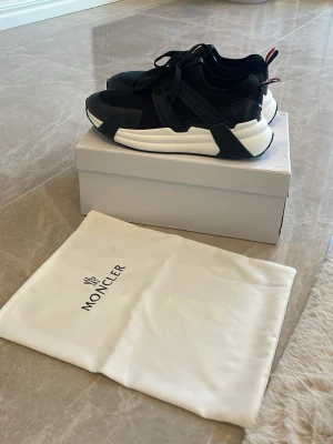 Svarta sneakers från Moncler - Snygga svarta sneakers från Moncler med chunky vit sula och svarta detaljer. Skorna har en modern design med svarta snören och Moncler-logga på hälen. Tillverkade i en mix av textil och syntetmaterial för en sportig och stilren look.  ‼️Pris kan diskuteras vid snabb affär‼️