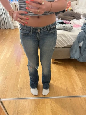 Blåa lågmidjade jeans från Replay - Säljer ett par blåa lågmidjade jeans från Replay med slitningar och hål på ena knät. Jag är 160 och jeansen är stl xs
