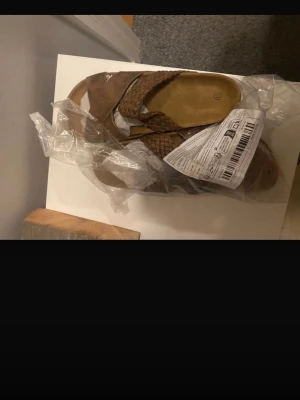 Bruna sandaler med flätad rem - Säljer ett par helt nya tofflor som jag provat en gång men de varit för stora, det är jätte sköna att gå i och är säkert bekväma att ha på jobbet eller bara hemma och ute på sommaren, de är helt nya men har dock inte kvittot kvar på de. 
