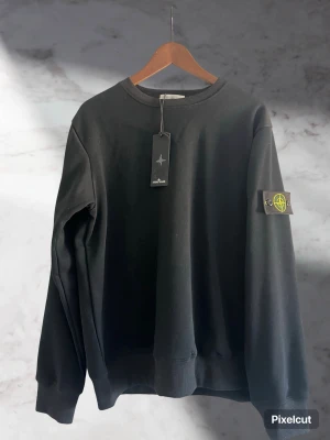 Svart sweatshirt från Stone Island - Svart sweatshirt från Stone Island. Tröjan har den ikoniska logotypen på vänster ärm och är tillverkad i mjukt bomullsmaterial. Tröjan är storlek L men passar mig som har mellan M och L bra. Pris kan självklart diskuteras✅🤝