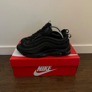 Nike Air Max 97 Triple Black - Nike Air Max 97 Triple Black sneakers med ikoniska vågformade paneler och synlig Air-sula. Helt svarta med reflekterande detaljer och klassisk snörning. Ovandel i textil och syntet, perfekt för en clean och sportig look. Äkta såklart, för frågor skriv privat