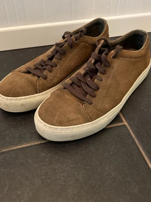 Bruna mockasneakers med vit sula - Säljer ett par bruna sneakers i mocka med mörkbruna skosnören och vit, tjock gummisula. Klassisk låg modell med enkel design som passar till det mesta. Skorna har en stilren look och är perfekta för dig som gillar en avslappnad men snygg stil.