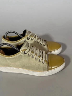 Beige sneakers med lackad tå - Stilrena Lanvins i beige mocka med glansig, lackad tå i olivgrönt. Skorna har vita snören, vita sulor och diskreta sömmar. Perfekta för dig som gillar en unik twist på klassiska sneakers.