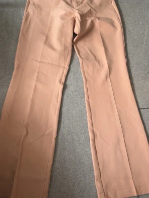 Beiga kostymbyxor från Bik Bok - Snygga beiga kostymbyxor från Bik Bok i rak modell. Byxorna har pressveck och hällor för skärp, vilket ger en stilren look. Perfekta att matcha med en kavaj eller en enkel topp. Materialet känns mjukt och följsamt.